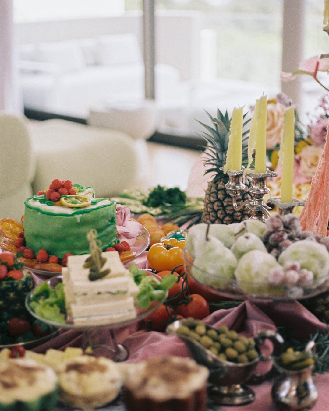 Decorative table setting with cakes, fruits, and candles in a bright room.