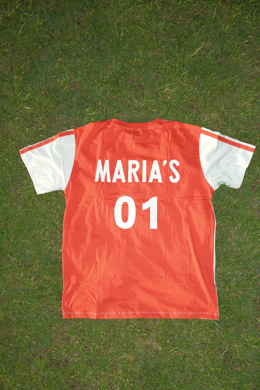 Back of a football sports jersey with “MARIA’S 01” printed on it, laid flat on grass.