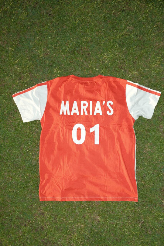 Back of a football sports jersey with “MARIA’S 01” printed on it, laid flat on grass.