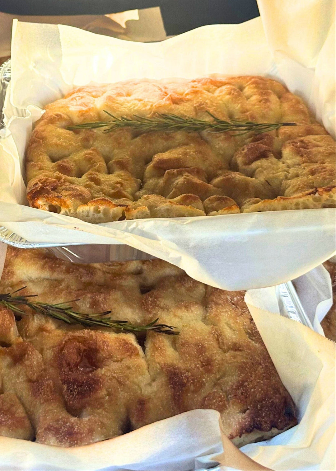 Two square bread loaves with rosemary on top, wrapped in white paper.